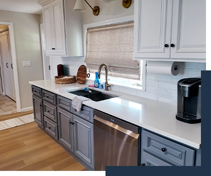 photo of a renovated kitchen in a Port Clinton lake house: the space features white subway tile backsplash, marble countertops, and cabinetry that is white above the counter and a dusty grey blue below the counter (featured image: Ode Custom Renovations homepage - your Cleveland home renovation specialists)