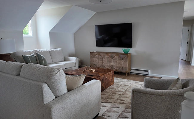 photo of the conversation den in a lake house in Port Clinton, Ohio: the space features wood floors, neutral grey furniture, dark wood accent pieces, and a textured, geometric rug
