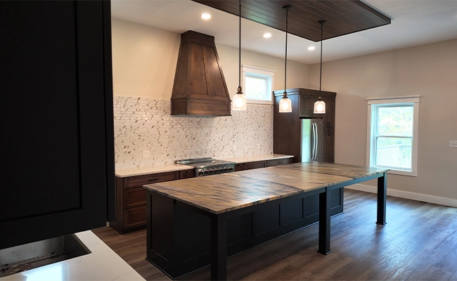 photo of one of Ode Custom Renovations' Cleveland home renovation projects: a modern renovated kitchen with dark wood cabinets, a large island with woodgrain countertop, stainless steel appliances, and pendant lighting to create a warm, contemporary feel